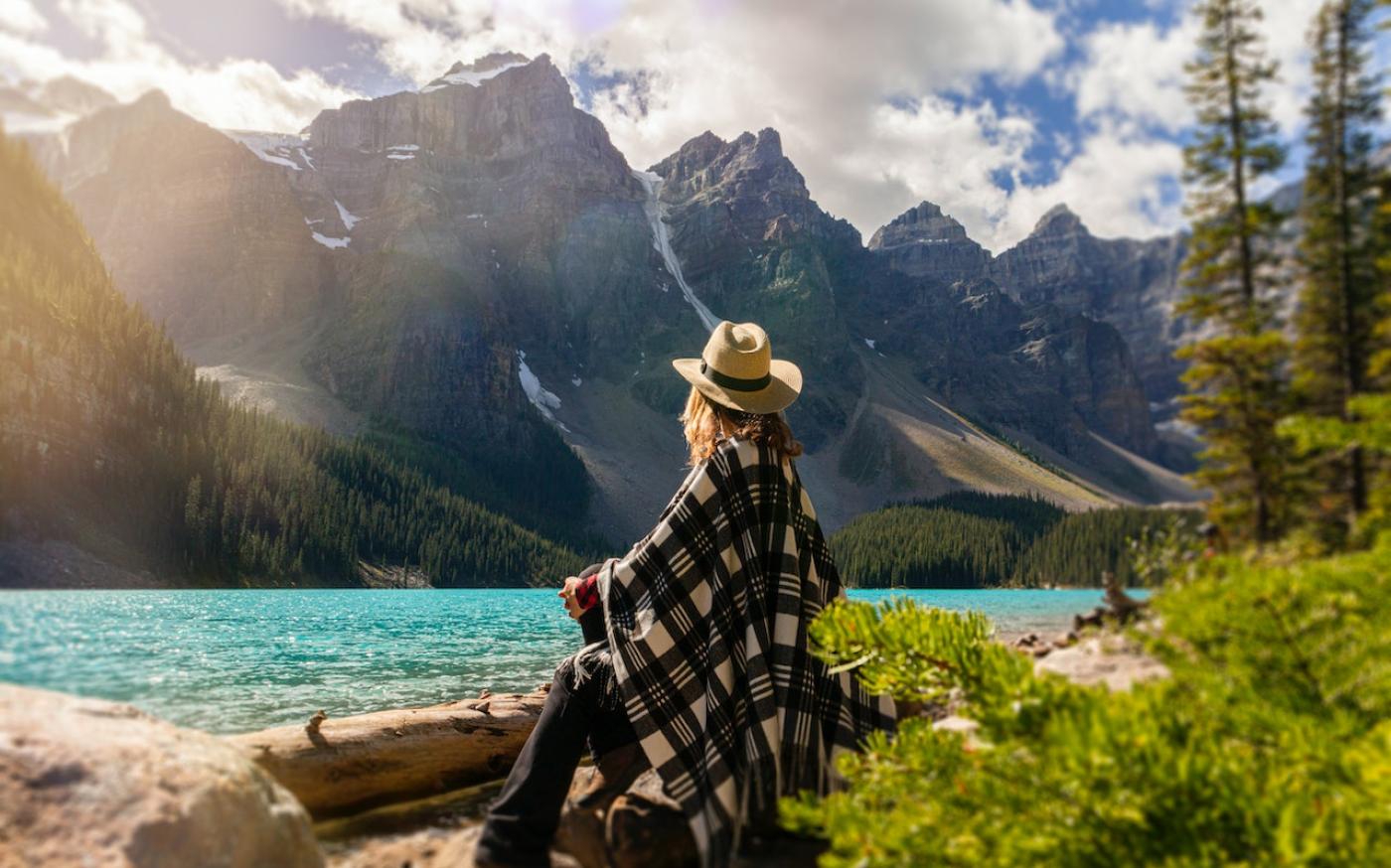 Woman sitting on a rock looking out at lake. In the distance is a large mountain range